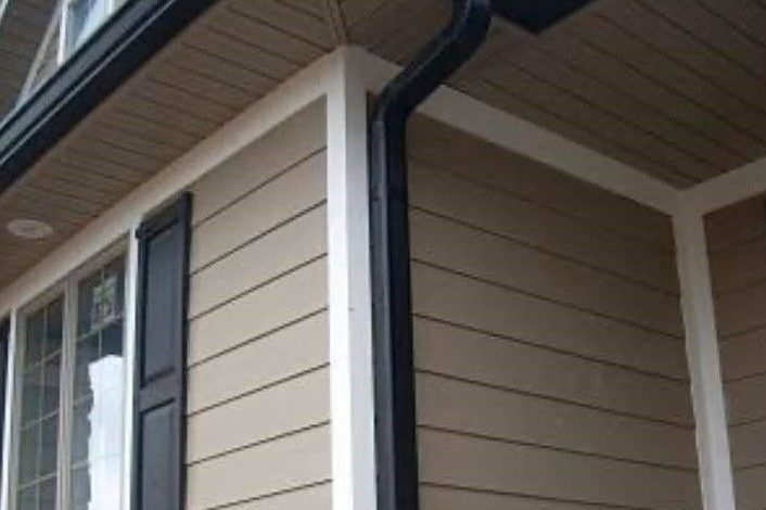 New black gutters and downspout on a home with tan siding